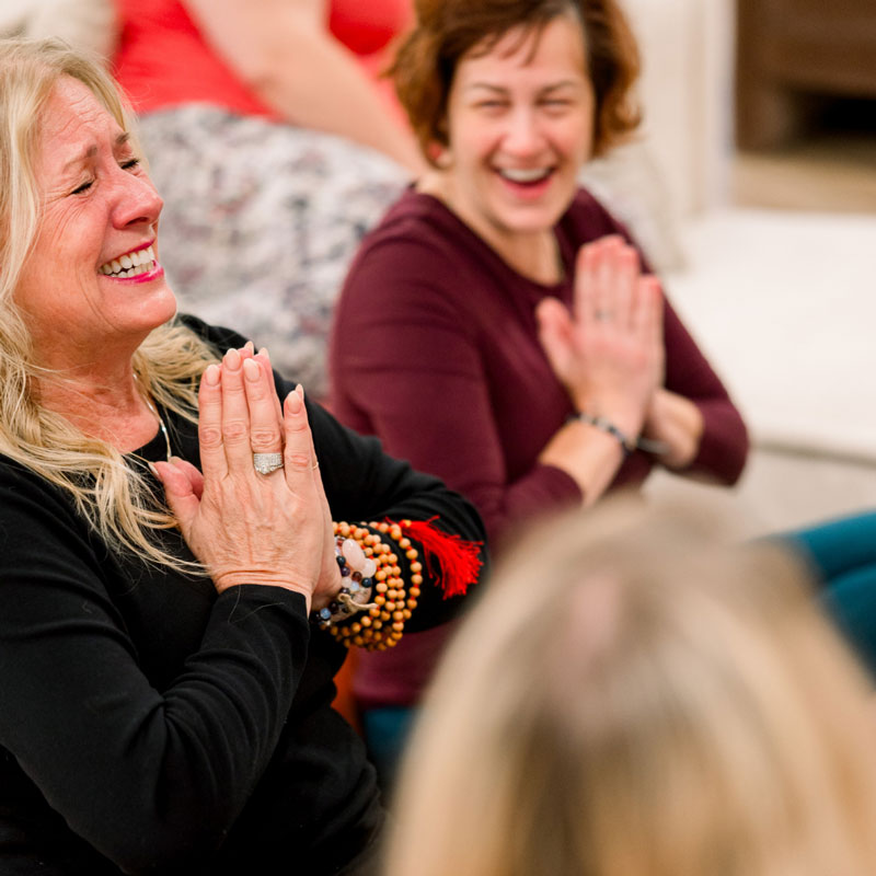 Two woman laughing with hands in prayer.