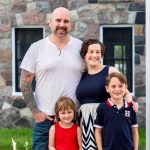 Woman & man with two kids in front of stone house.