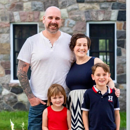Woman & man with two kids in front of stone house.