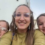 Woman with glasses and two girls resting on her shoulders.